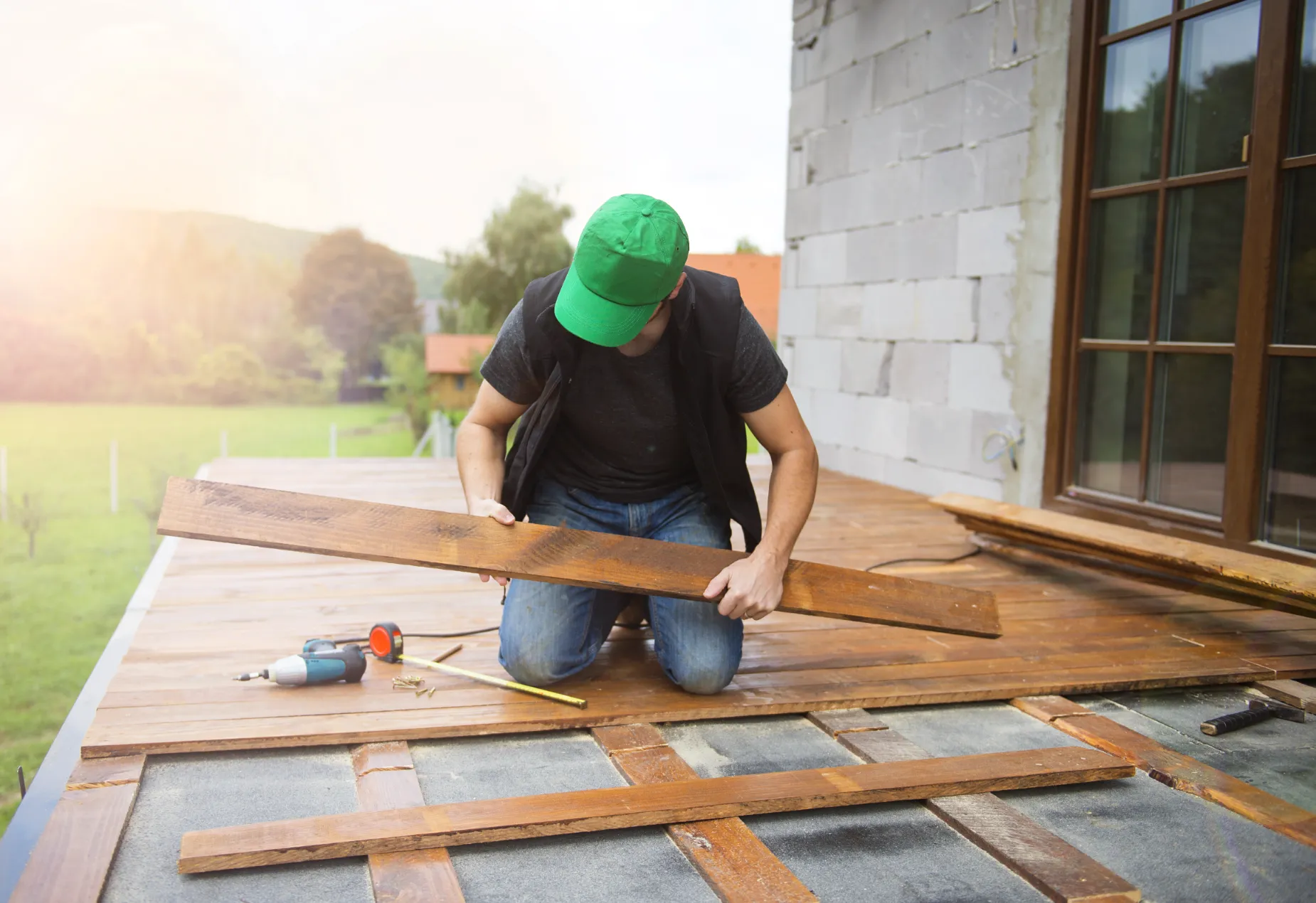 Builder wearing a hardhat constructing a wooden deck on a suburban house.