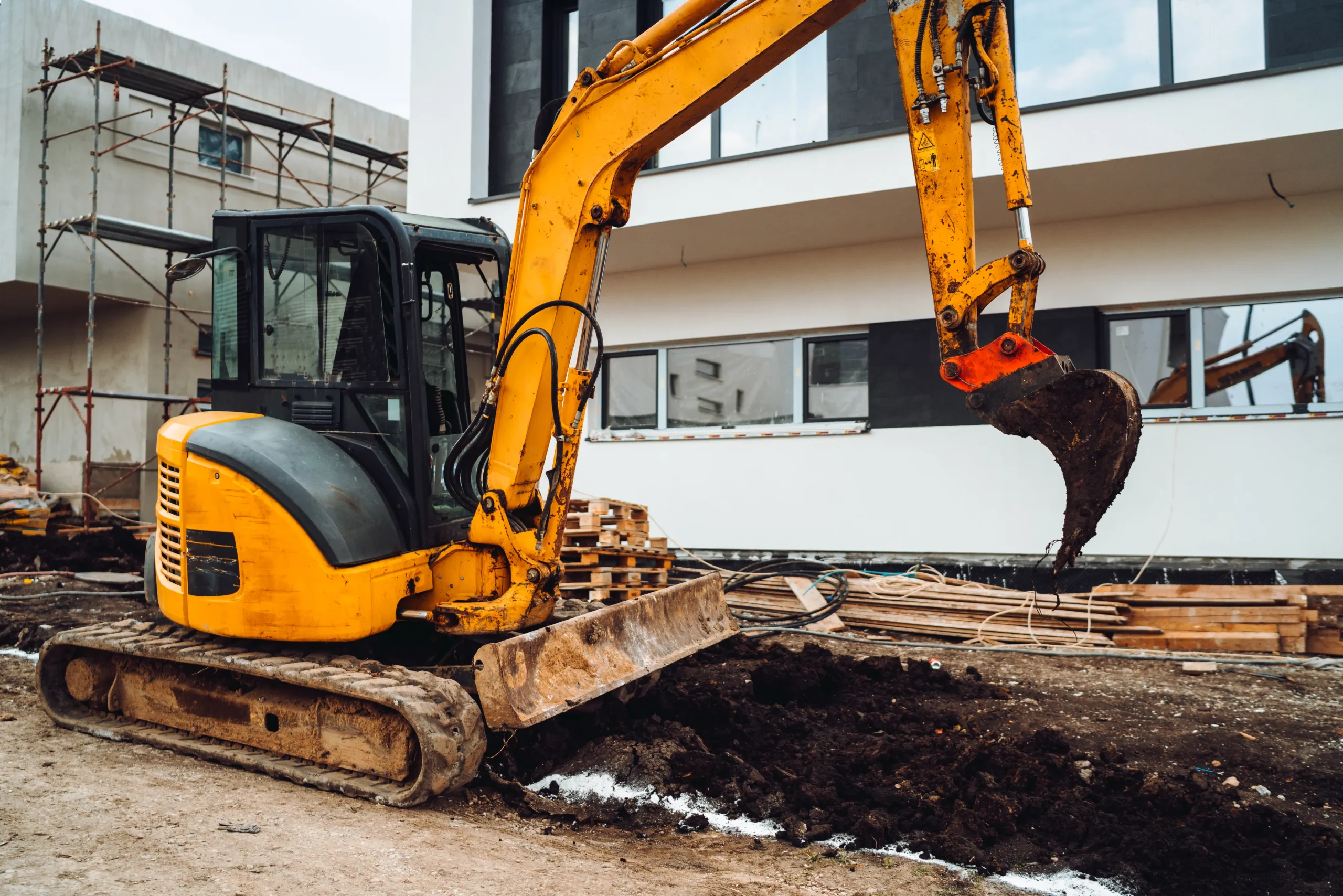 Active earthmoving construction site featuring heavy excavators and dirt piles around a foundation area.