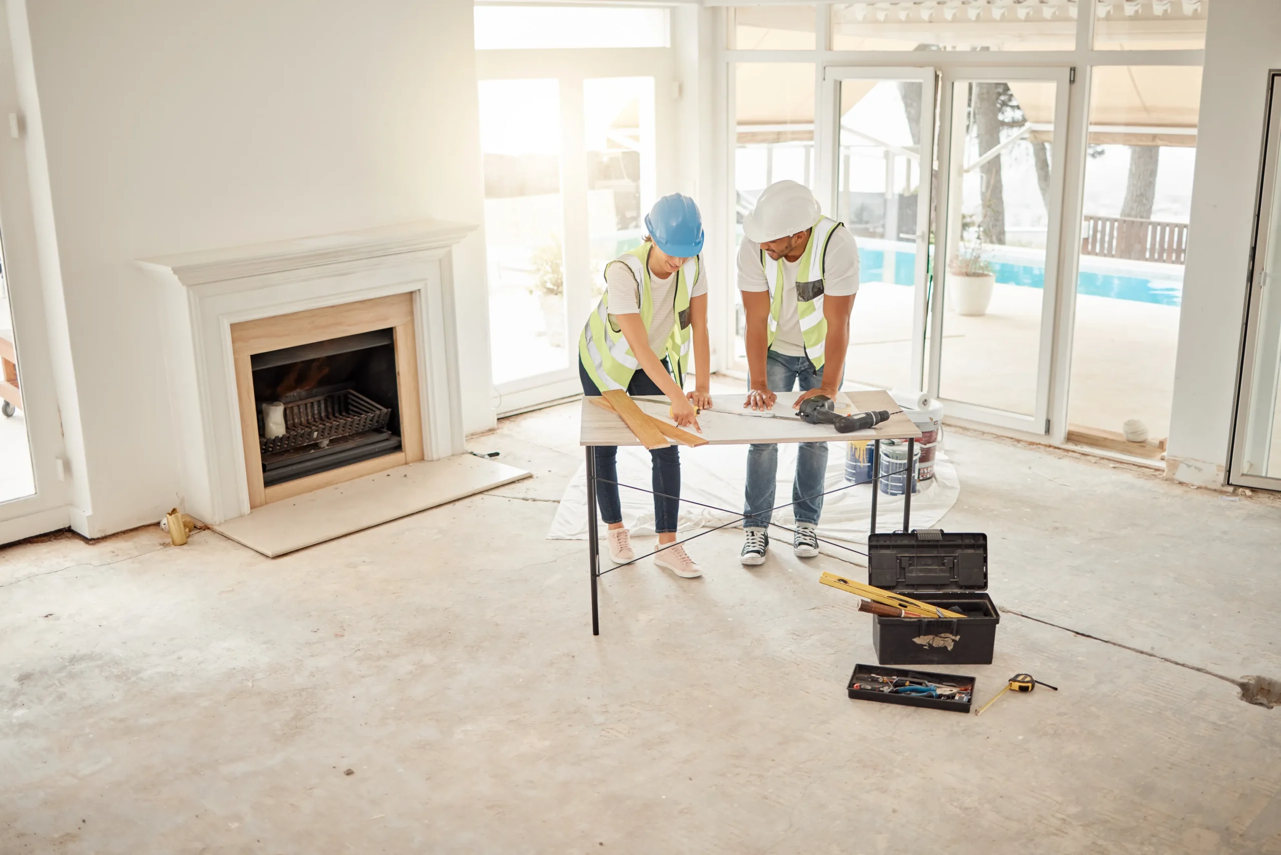 Two construction contractors reviewing blueprints and structural elements inside a building framing site.