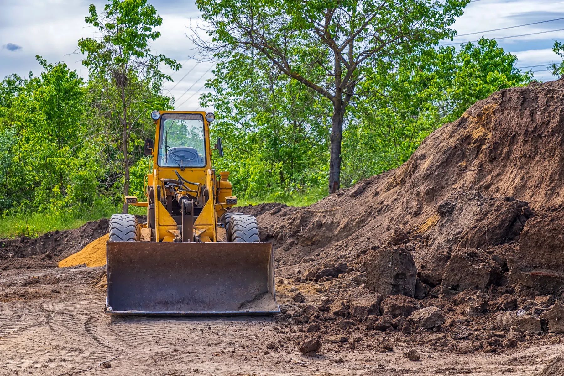 Earthmover working on a dirt hill set against a scenic rural landscape.