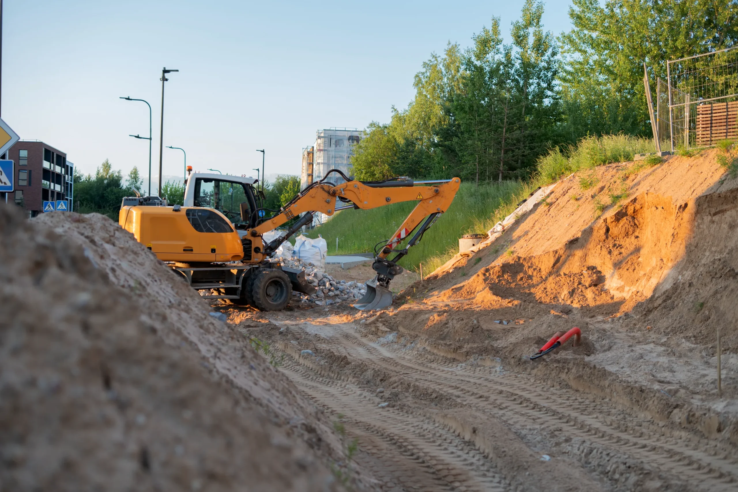Yellow excavator performing site preparation in an urban construction zone.
