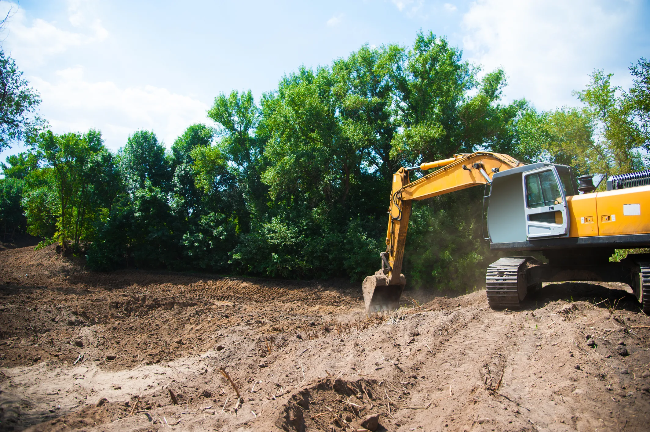 Excavator bucket scooping up dark topsoil on an active earth-moving project site.