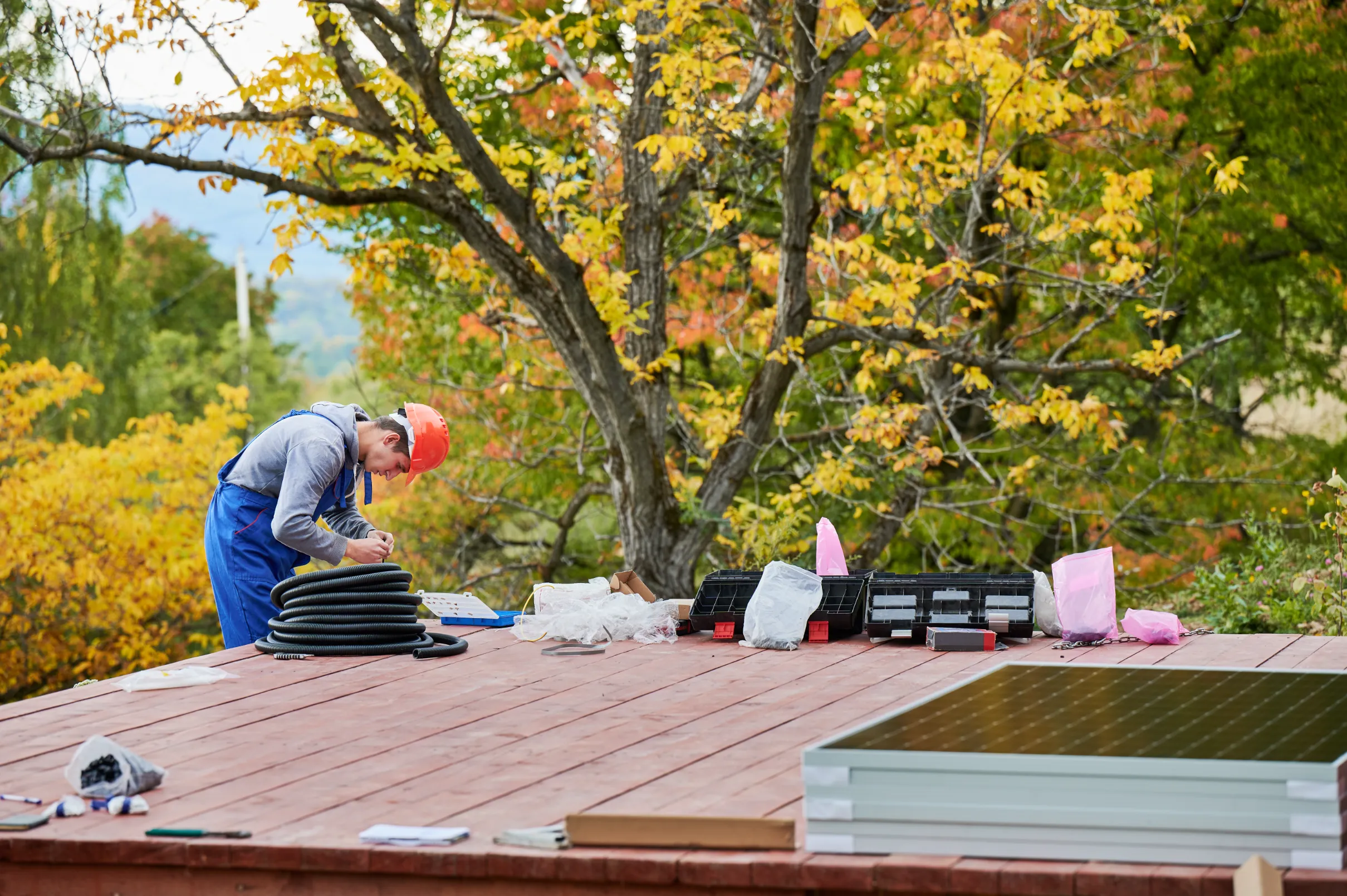 Worker wearing safety gear installing solar panels on a residential roof.